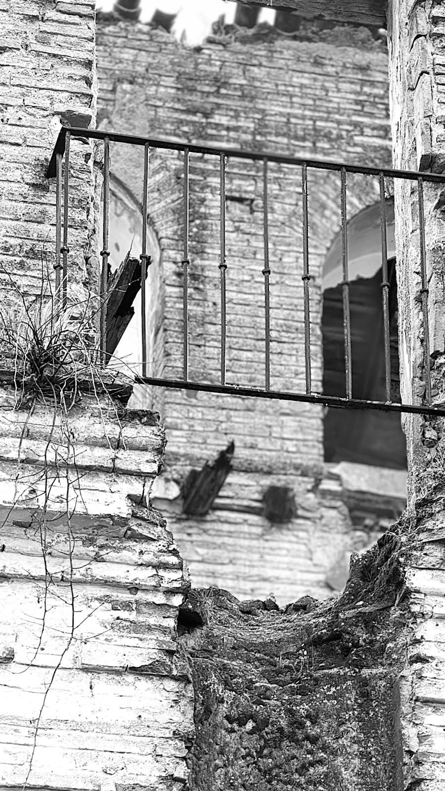Balcón de hierro sobre muros derruidos, en blanco y negro